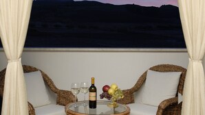 Un balcón con sillas de mimbre, una mesa de vidrio y una botella de vino.
