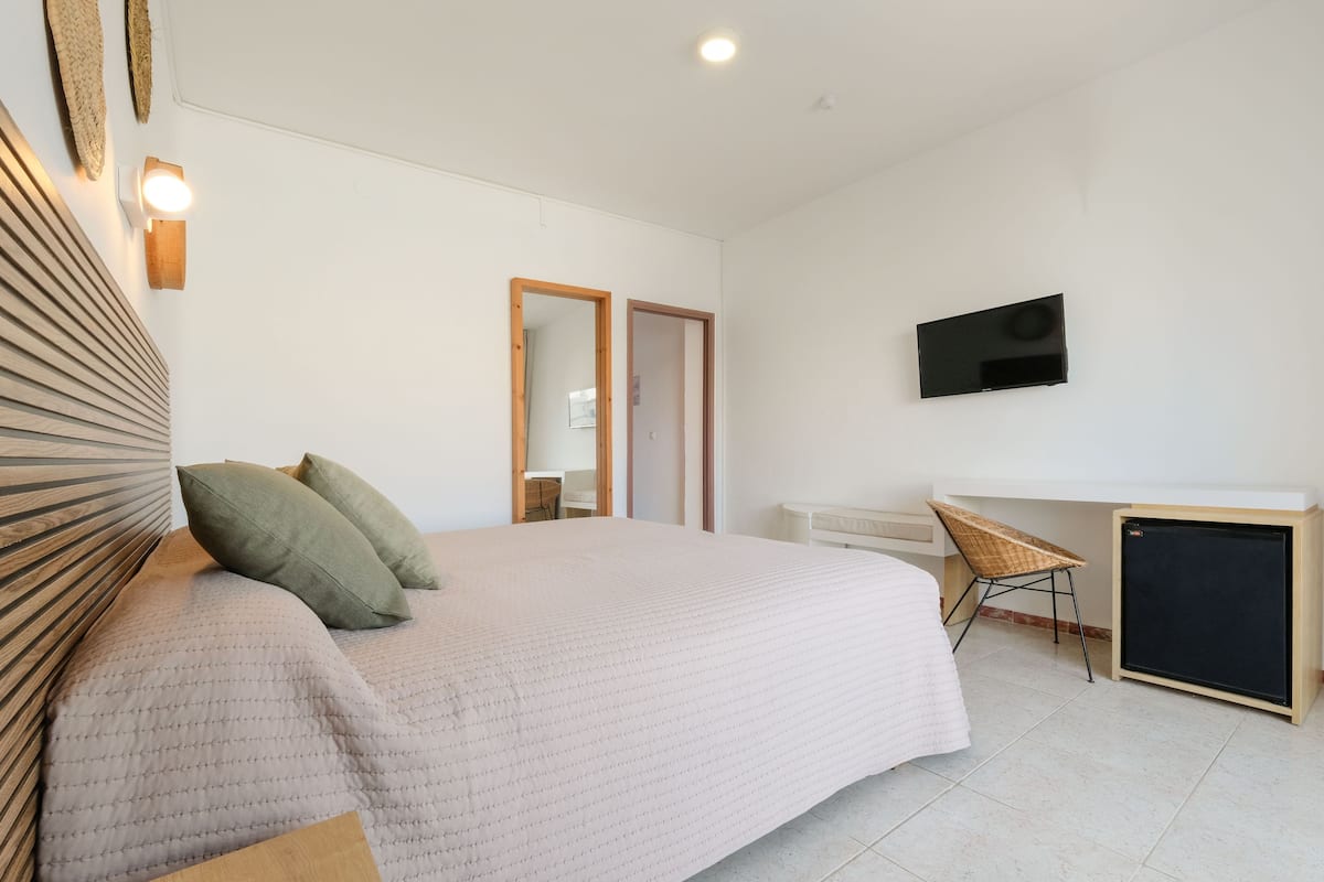 A bedroom with a large bed, a desk, a chair, and a television on the wall.