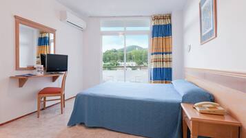 A hotel room with a bed, a desk with a computer, a chair, a telephone, and a window with curtains.