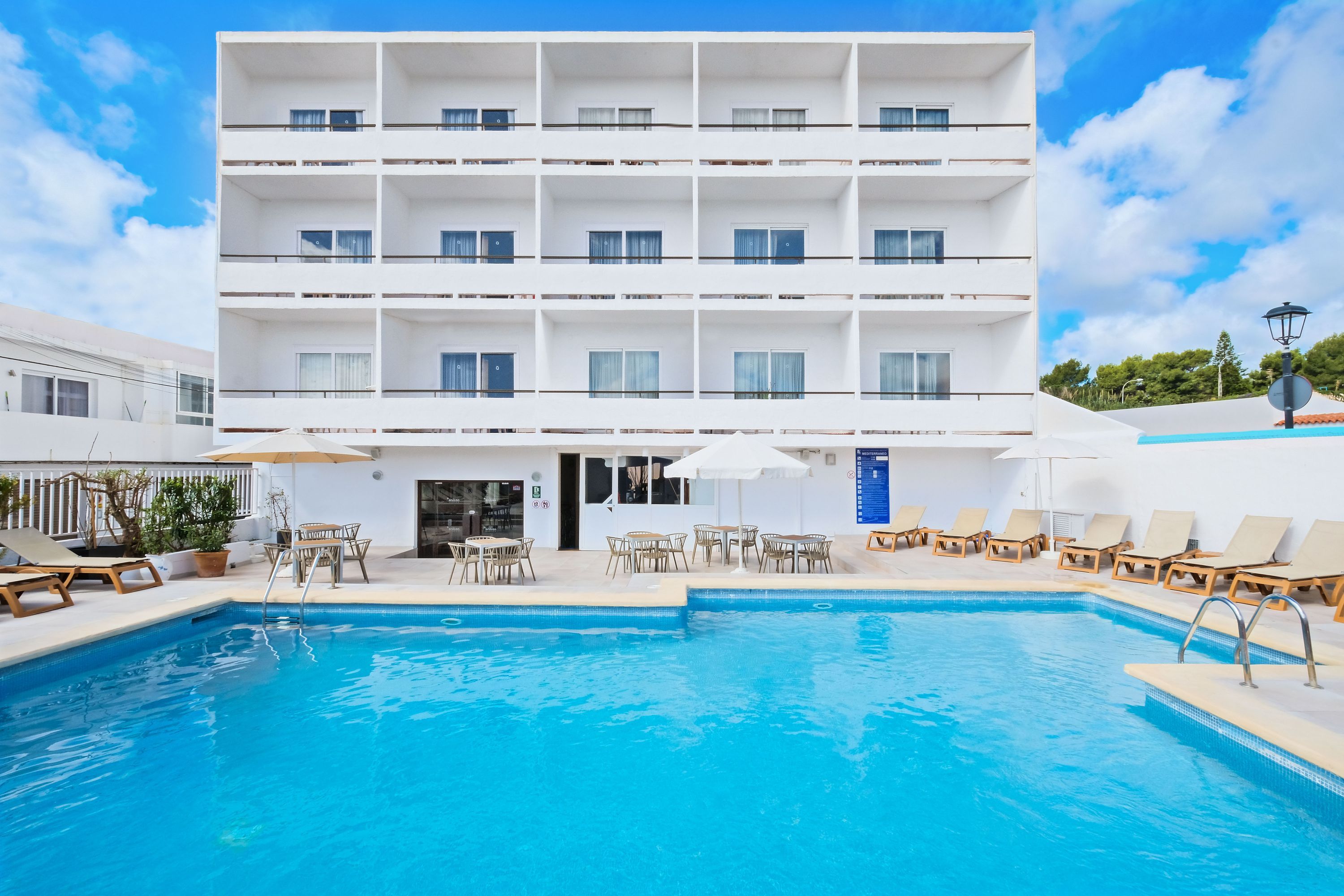 Een meerlaags hotel met een zwembad, terras en heldere lucht.