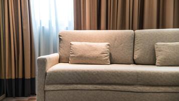 Un canapé beige avec deux coussins, dans une pièce où l’on peut voir des rideaux.