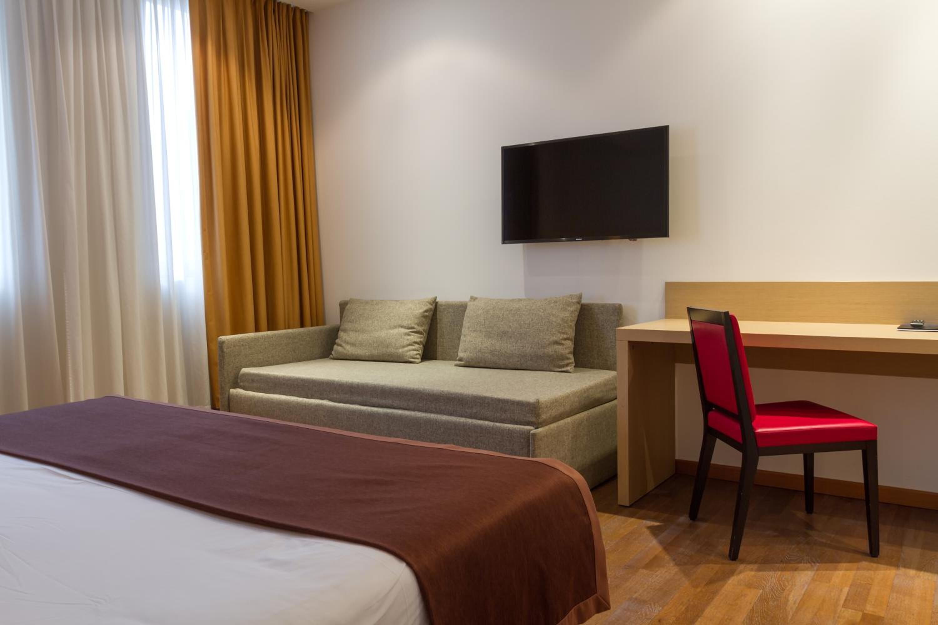A hotel room with a bed, a sofa, a desk, and a TV.