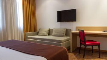 A hotel room with a bed, a sofa, a desk, and a TV.
