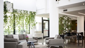 Um lobby moderno com um sofá cinzento, uma mesa de centro e uma área de refeições com cadeiras e uma mesa.