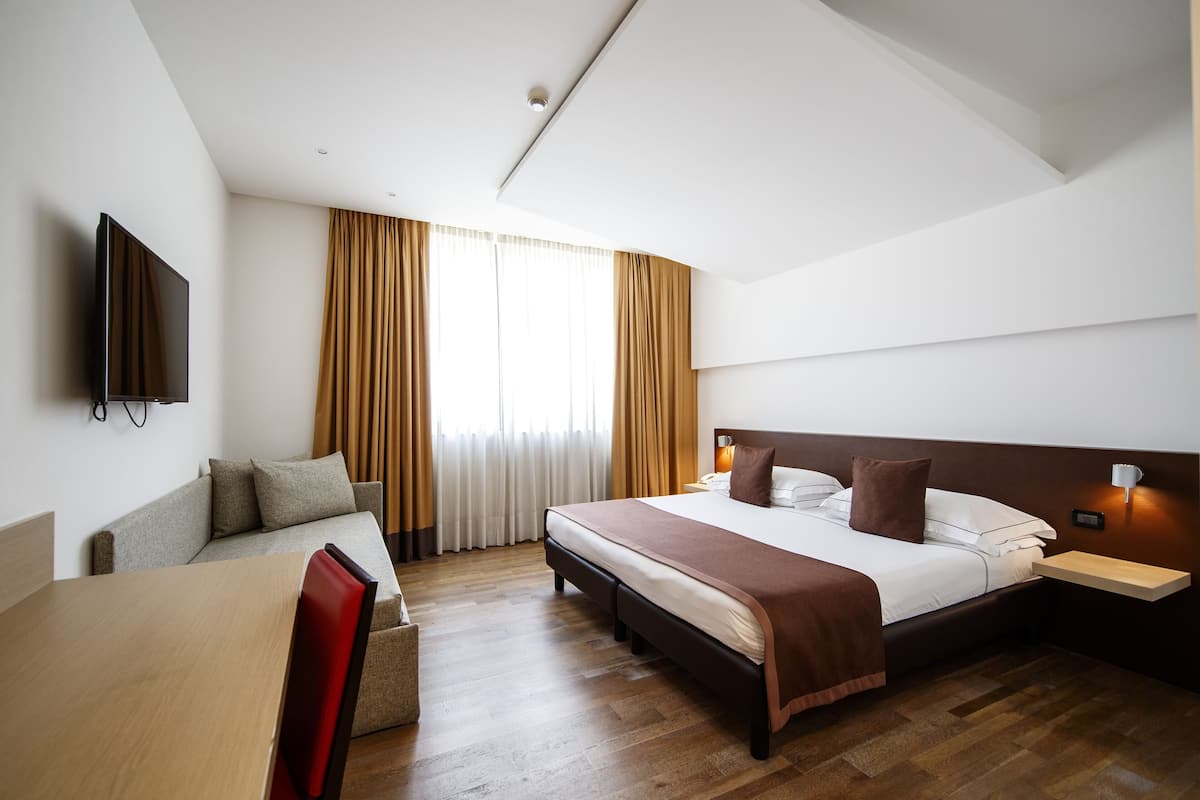 Een hotelkamer met een bed, nachtkastjes, een televisie, een sofa en een eettafel.