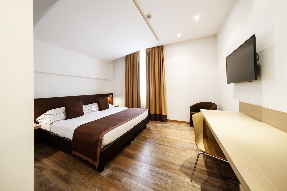 Een moderne hotelkamer met een groot bed, een bureau en een flatscreen televisie aan de muur.