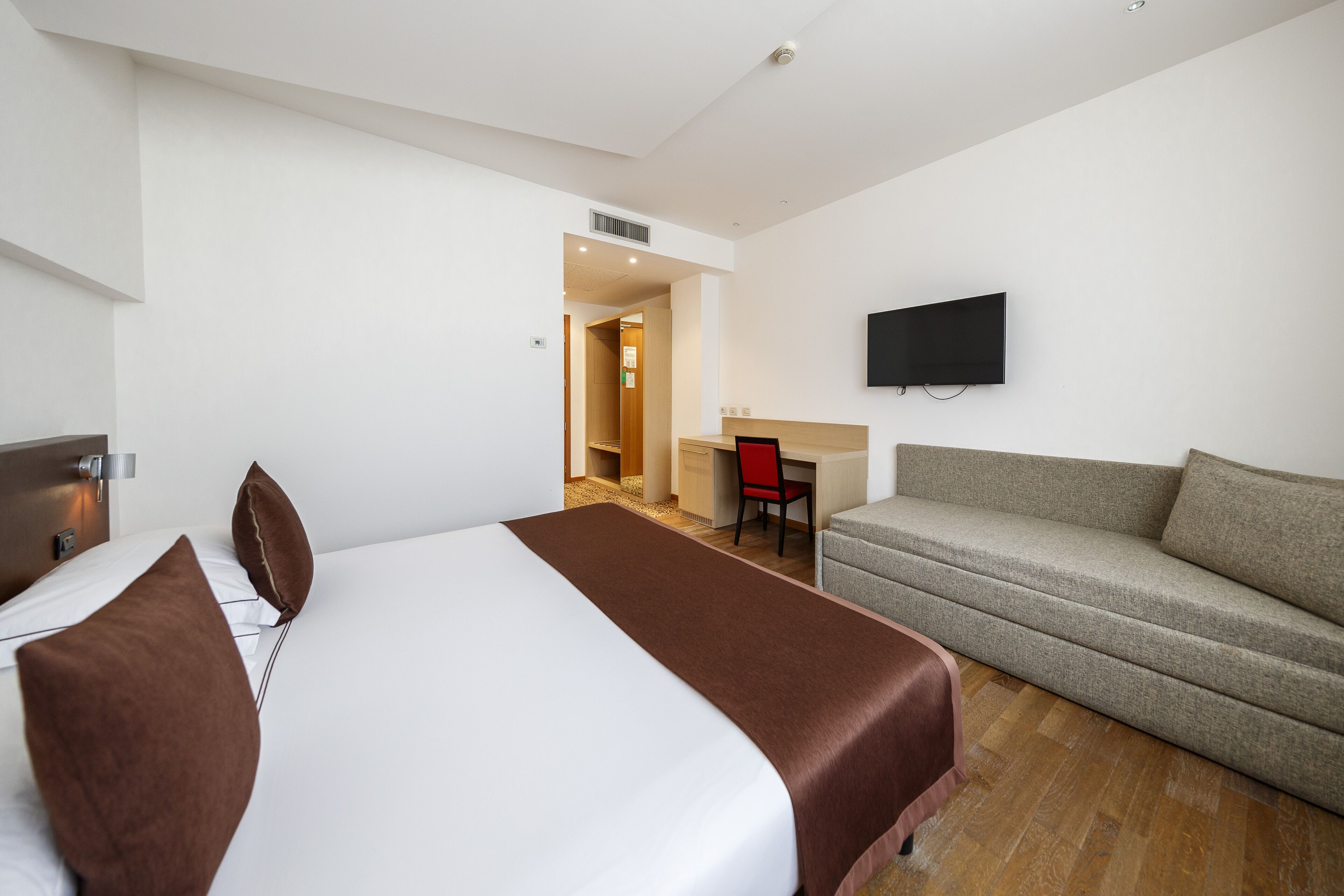 Una camera d'albergo con un letto grande, una poltrona, una scrivania e una televisione.