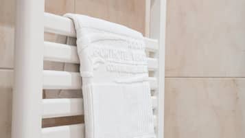A white towel hanging on a white towel rack in a bathroom with beige tiles.