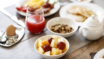 A breakfast table with various dishes including a bowl of fruit, a glass of red juice, and plates of food.