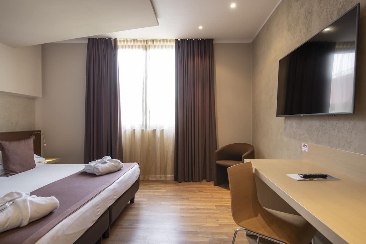 Een hotelkamer met een bed, bureau, stoel, televisie en raam met gordijnen.