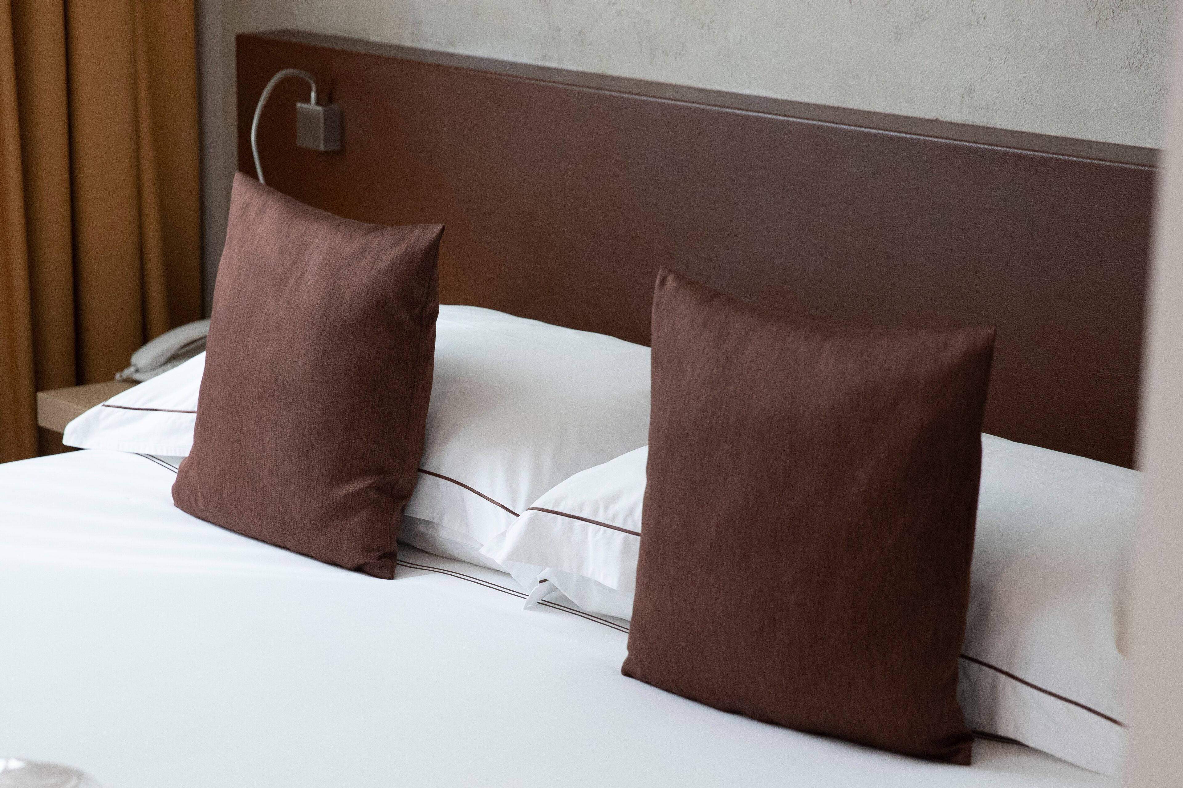 A neatly made bed with two brown pillows and a white comforter.