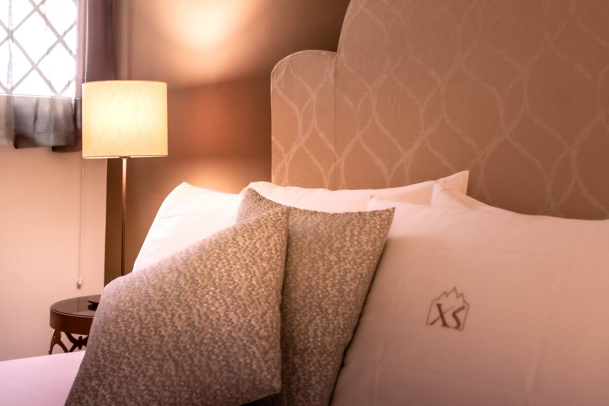 A neatly made bed with patterned pillows, a bedside lamp, and a wall with a geometric design.