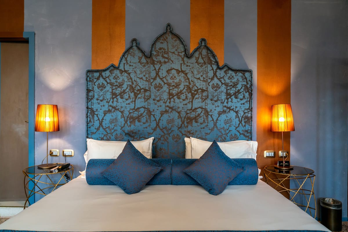 A neatly made bed with blue and white bedding, two bedside lamps, and a decorative headboard.