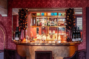A bar area with a variety of liquor bottles and glasses, a mirror reflecting the bar, and a decorative garland.