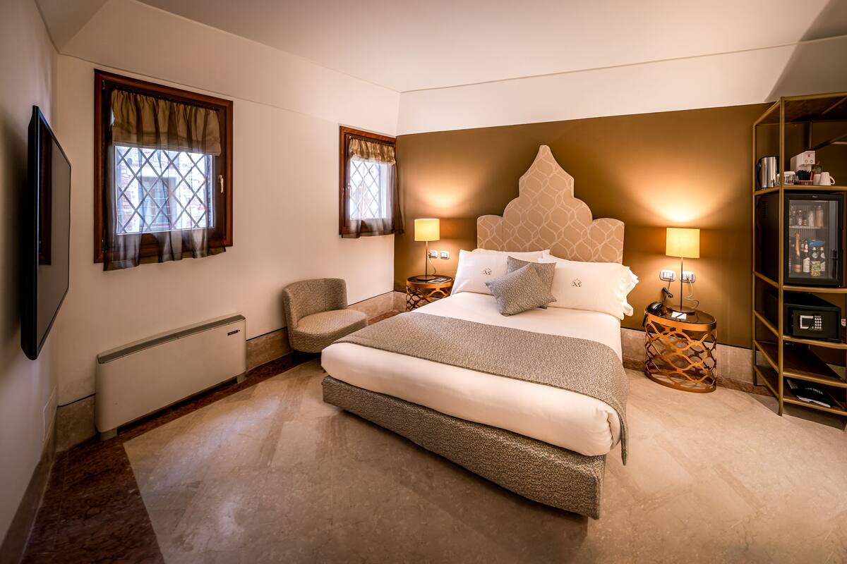 A bedroom with a large bed, two bedside tables with lamps, a chair, a television, and a bookshelf.