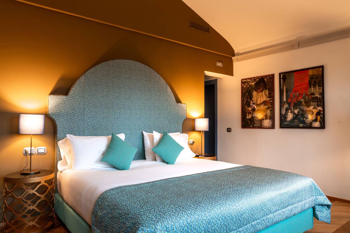 A hotel room with a large bed, two bedside lamps, and artwork on the wall.