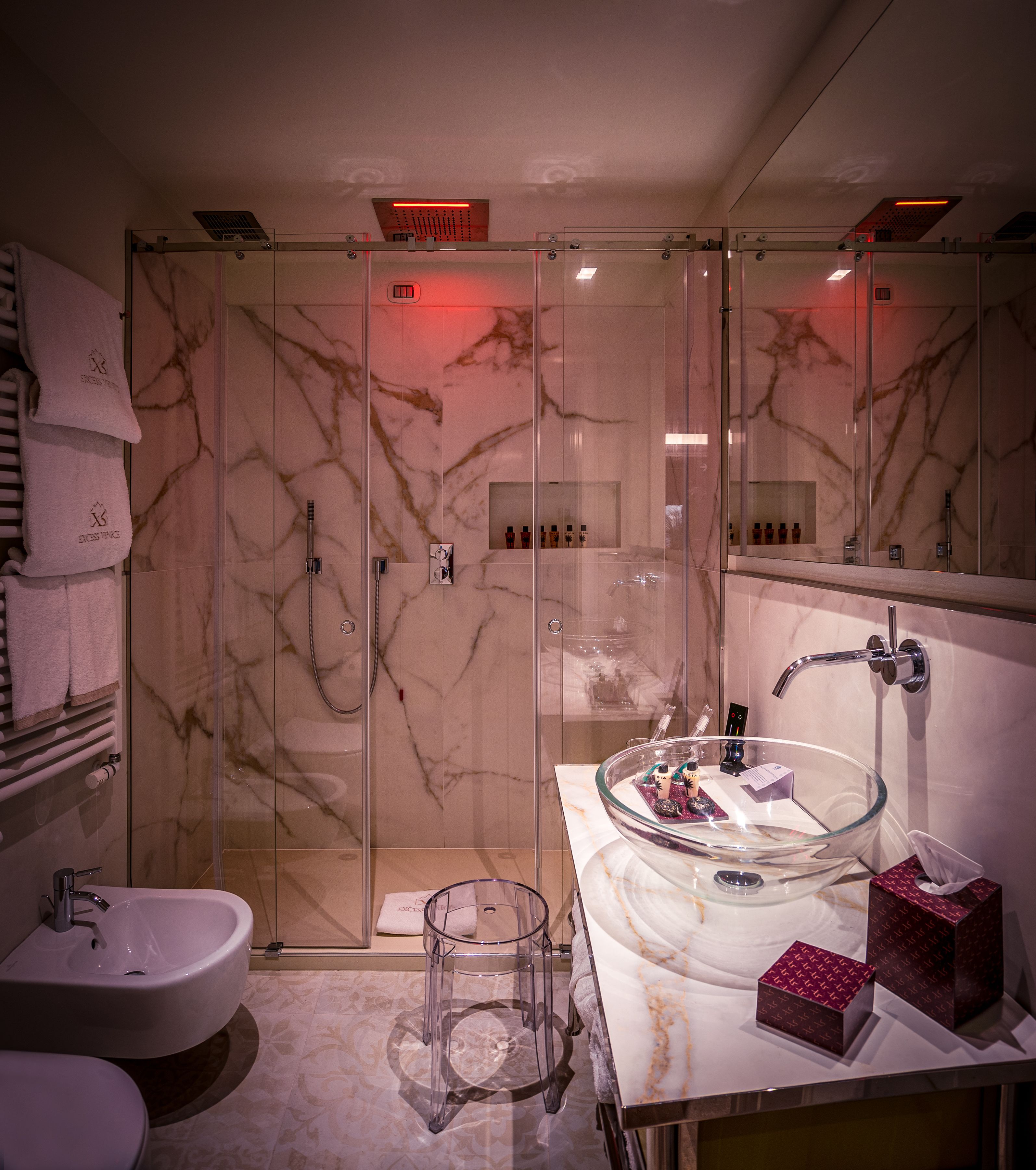 Un baño moderno con ducha envuelta en vidrio, lavamanos de cristal y tocador con artículos de aseo.