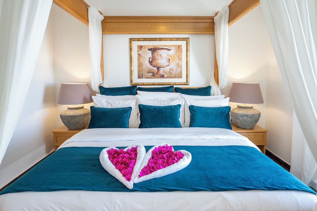 A neatly made bed with a heart-shaped flower arrangement, teal and white bedding, and a framed picture on the headboard.