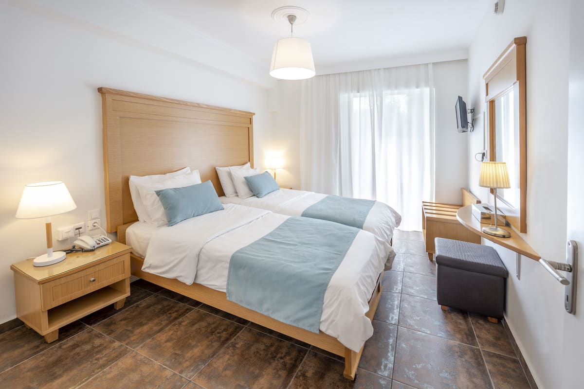 A double bed with a wooden headboard, a bedside table with a lamp, and a small bench.
