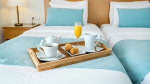 Una cama bien tendida con una bandeja de desayuno que incluye croissants, café y zumo de naranja.