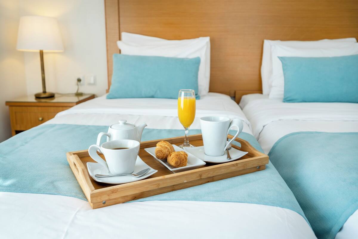 A neatly made bed with a tray of breakfast items including croissants, coffee, and orange juice.