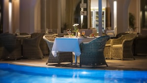 Un área de comedor al aire libre con mobiliario de mimbre y una piscina.