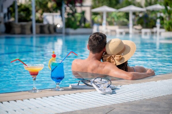 A poolside with lounge chairs, a glass of red cocktail, and a blue cocktail with a straw. - Peridis Family Resort (Kos)