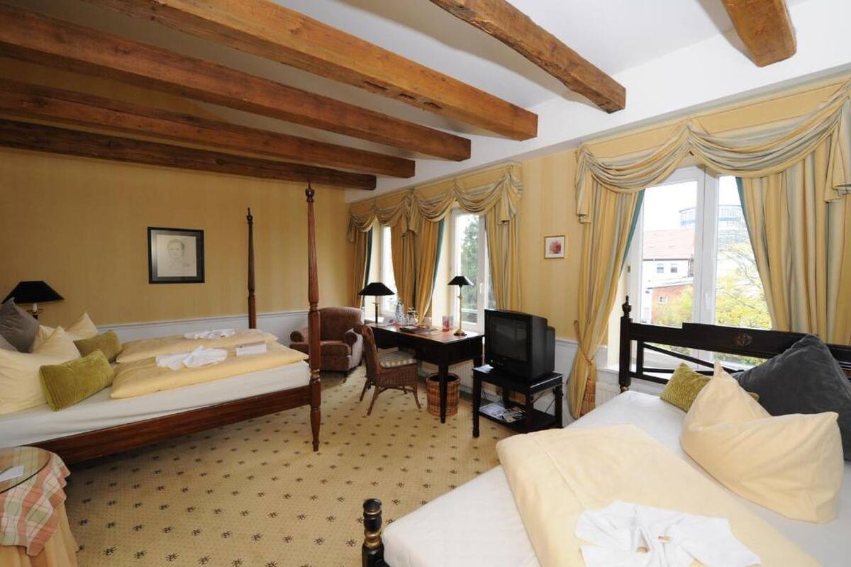 Une chambre d’hôtel avec un lit, un bureau avec une télévision, une chaise et une fenêtre avec des rideaux.