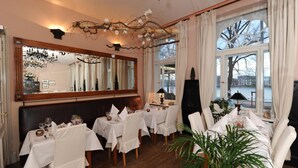 A dining area with white tablecloths, wooden chairs, a chandelier, and a large mirror. - Hotel Niederländischer Hof Schwerin (Schwerin)