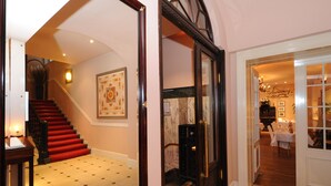 A grand staircase with red carpet leading to a landing, a large framed artwork on the wall, and a dining area with a chandelier. - Hotel Niederländischer Hof Schwerin (Schwerin)