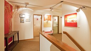 A hallway with a wooden bench, a vase with tall grasses, and framed artwork on the walls. - Hotel Lehmeier (Neumarkt in der Oberpfalz)