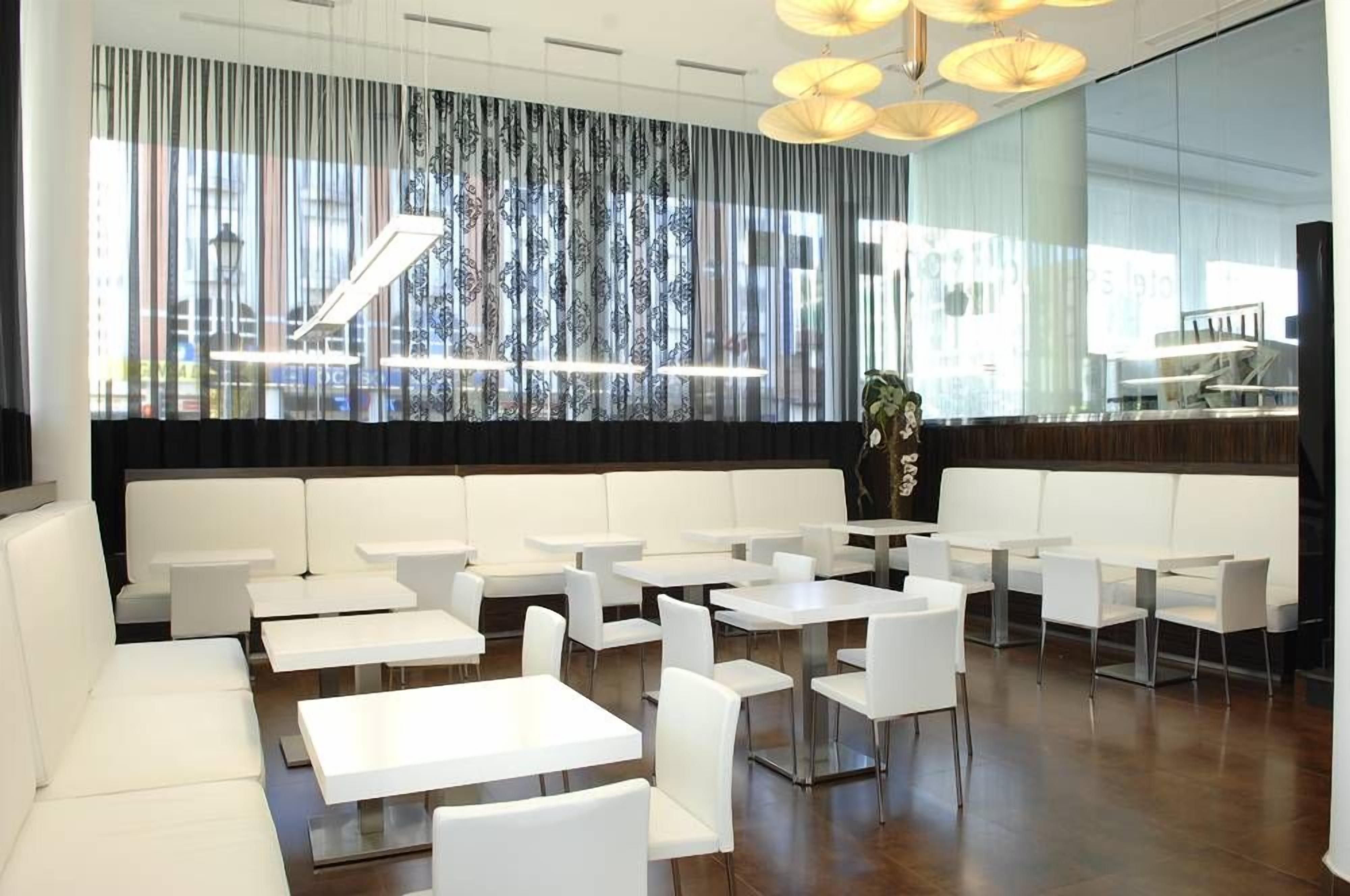 A modern interior with white seating and tables, a patterned curtain, and a view of the city.