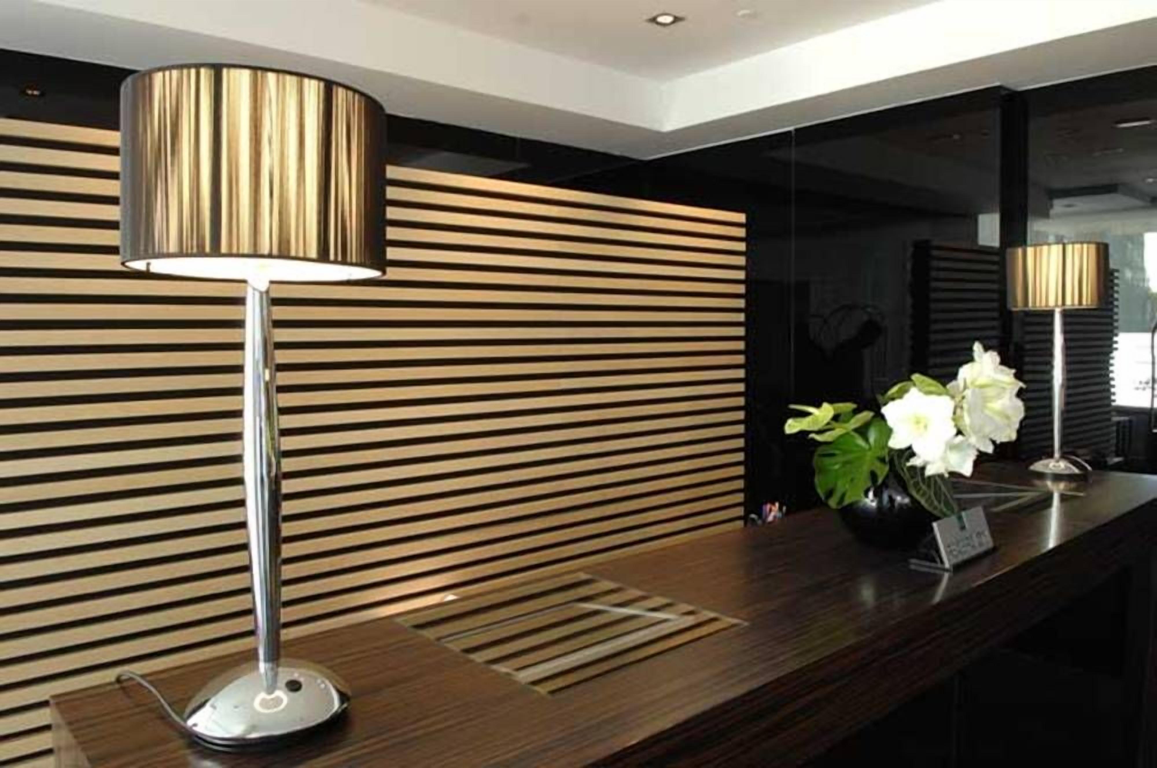 A reception desk with a modern lamp, a vase with flowers, and a wooden slatted wall.