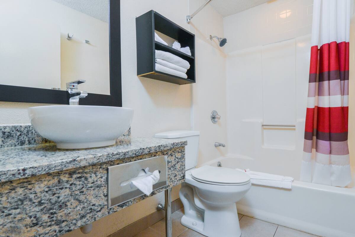 Un baño con lavamanos, espejo, toallero, inodoro y ducha.