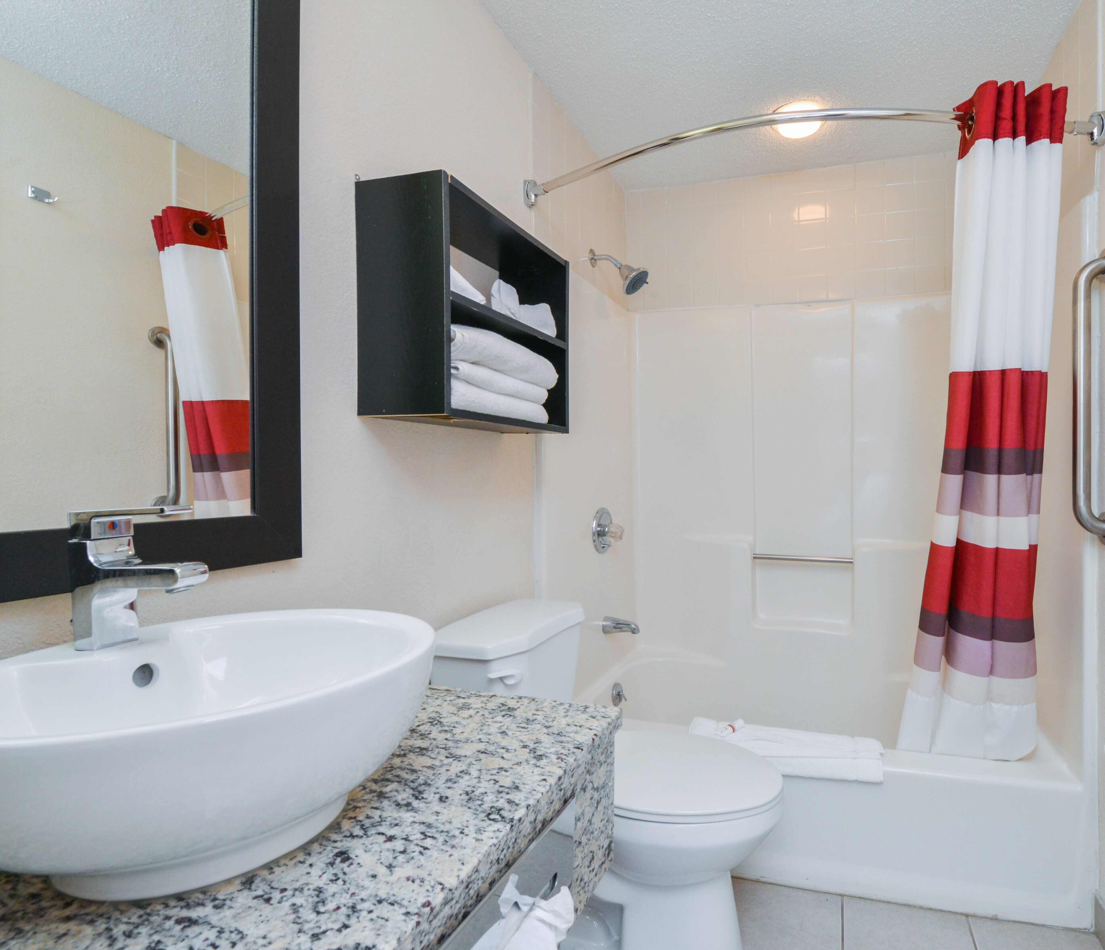 A bathroom with a white sink, toilet, and bathtub. There is a shower curtain with red and white stripes, and a mirror above the sink.