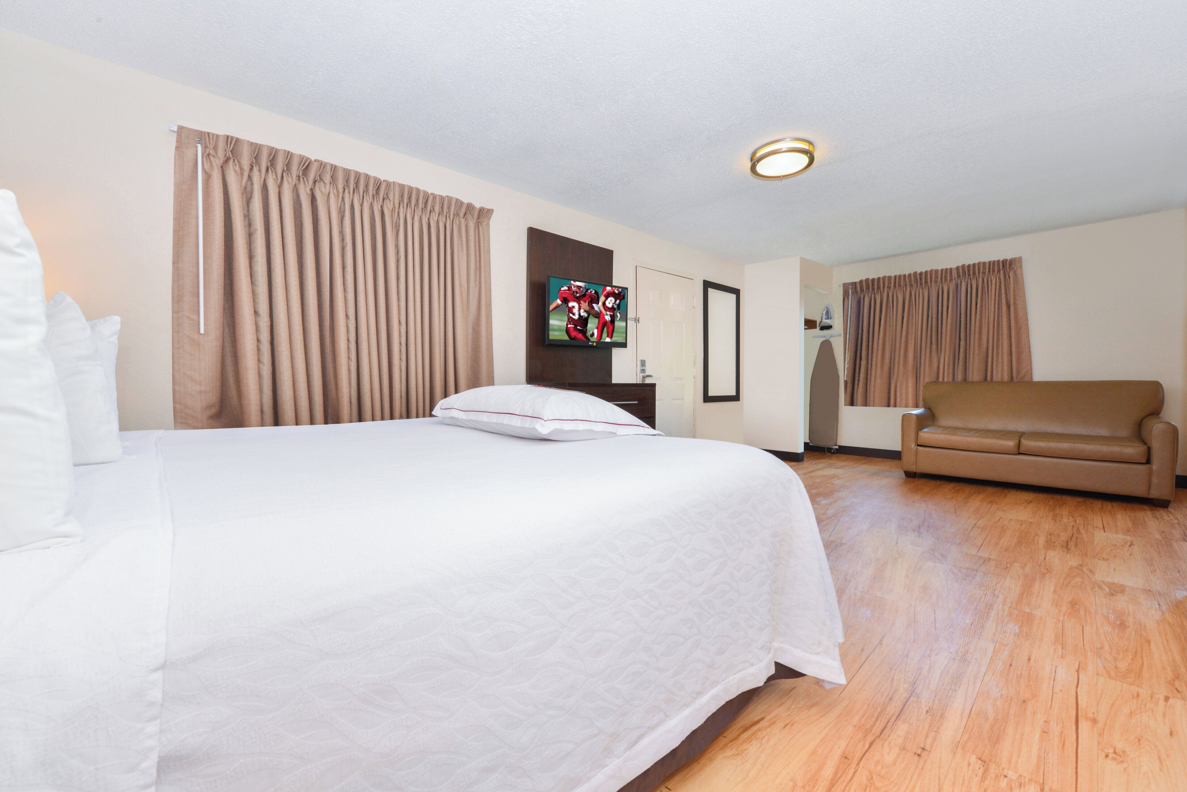 A hotel room with a large bed, a sofa, a television, and a ceiling light.