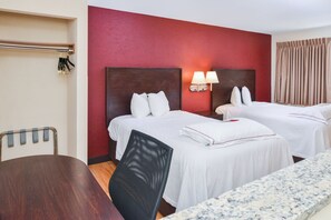 A hotel room with two beds, a wooden table, a chair, and a red accent wall. - Red Roof Inn PLUS+ & Suites Guilford (Guilford)
