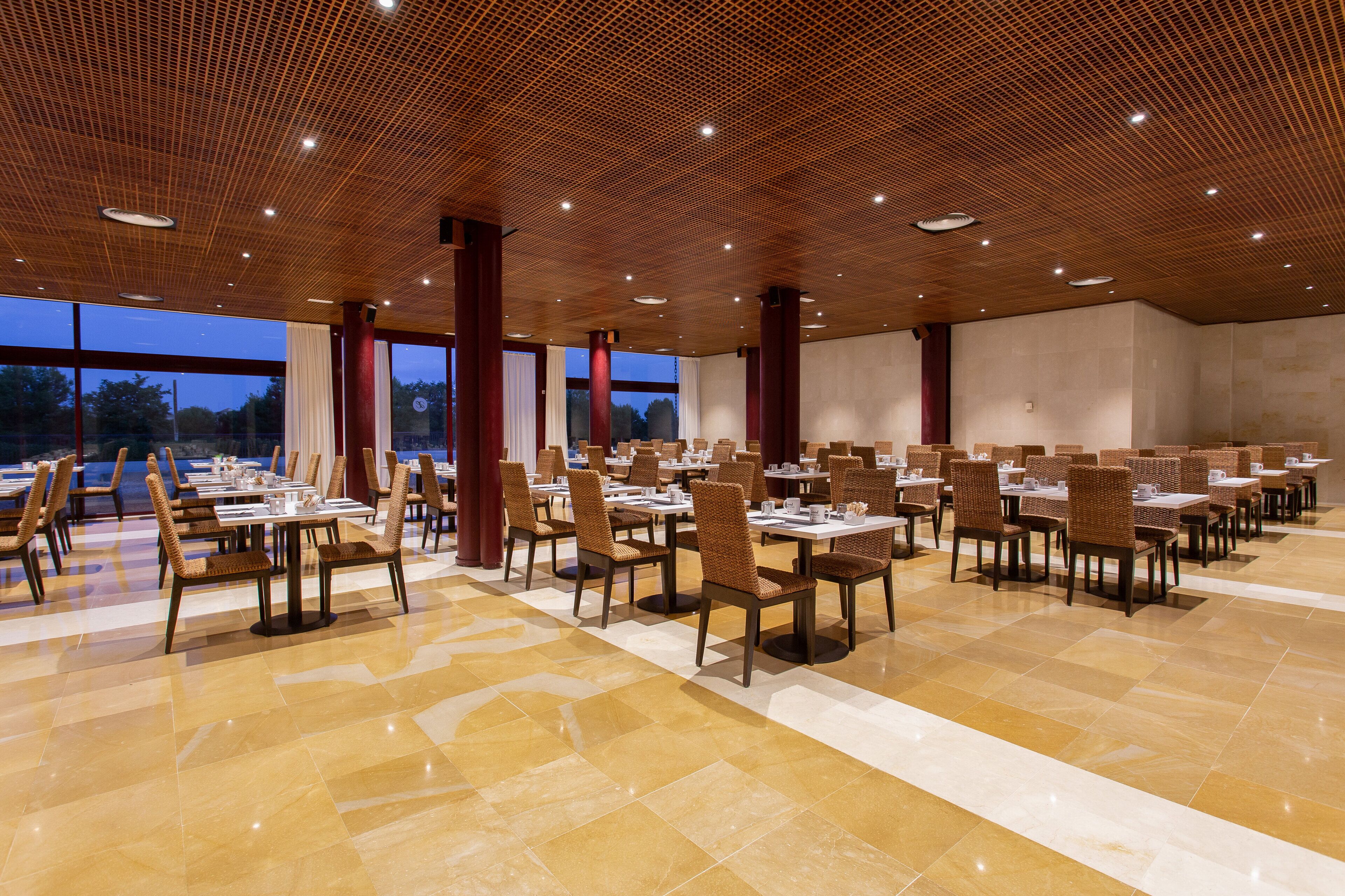 Un comedor amplio con varias mesas y sillas, ventanas grandes y techo de madera.