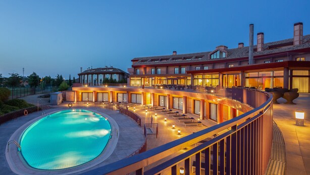 Un hotel con piscina, mobiliario exterior y una terraza bien iluminada.
