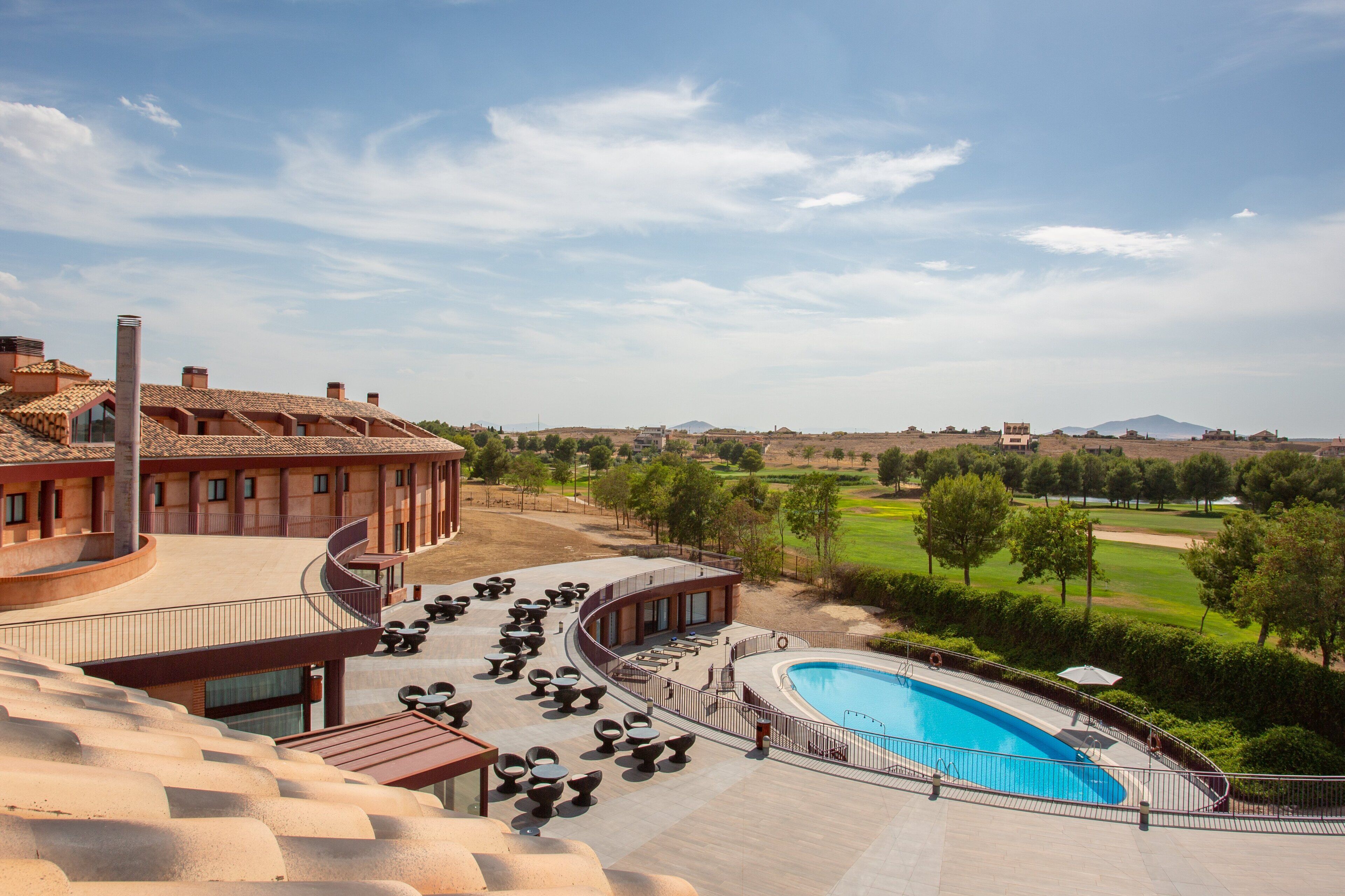 A pool area with lounge chairs and a swimming pool, surrounded by a landscaped garden and a building with a curved roof.