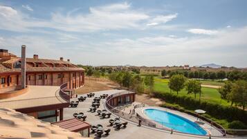 Area piscina con lettini e piscina, circondata da un giardino curato e un edificio con tetto curvo.