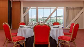 Un salón de conferencias con una mesa redonda, sillas rojas y vistas a un paisaje desértico a través de amplias ventanas.