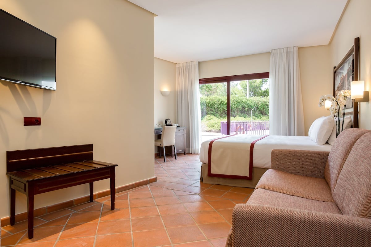 A hotel room with a bed, a sofa, a desk, and a TV mounted on the wall.