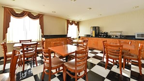 A dining area with a checkered floor, wooden chairs, a central table, and a kitchen area with appliances and cabinets.