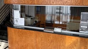 A reception desk with a wooden finish, a glass partition, and a sign requesting mask-wearing.