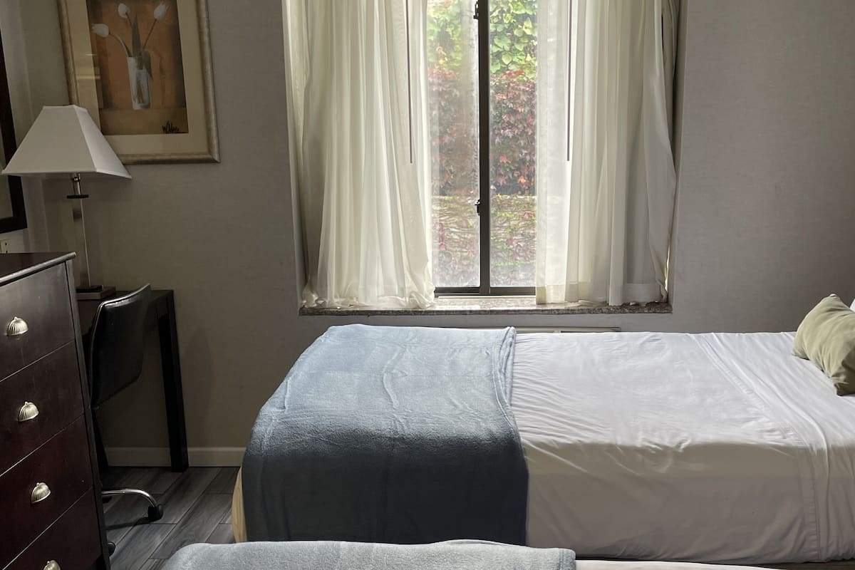 A hotel room with two beds, a dresser, a lamp, and a window with curtains.