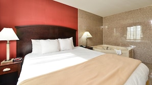 A hotel room with a large bed, two bedside lamps, a nightstand, a bathroom with a sink and mirror, and a red accent wall.