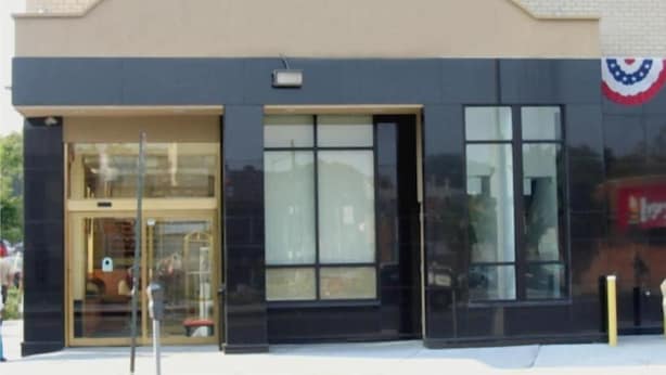 A building with a large glass entrance, a black awning, and a flag on the right side.