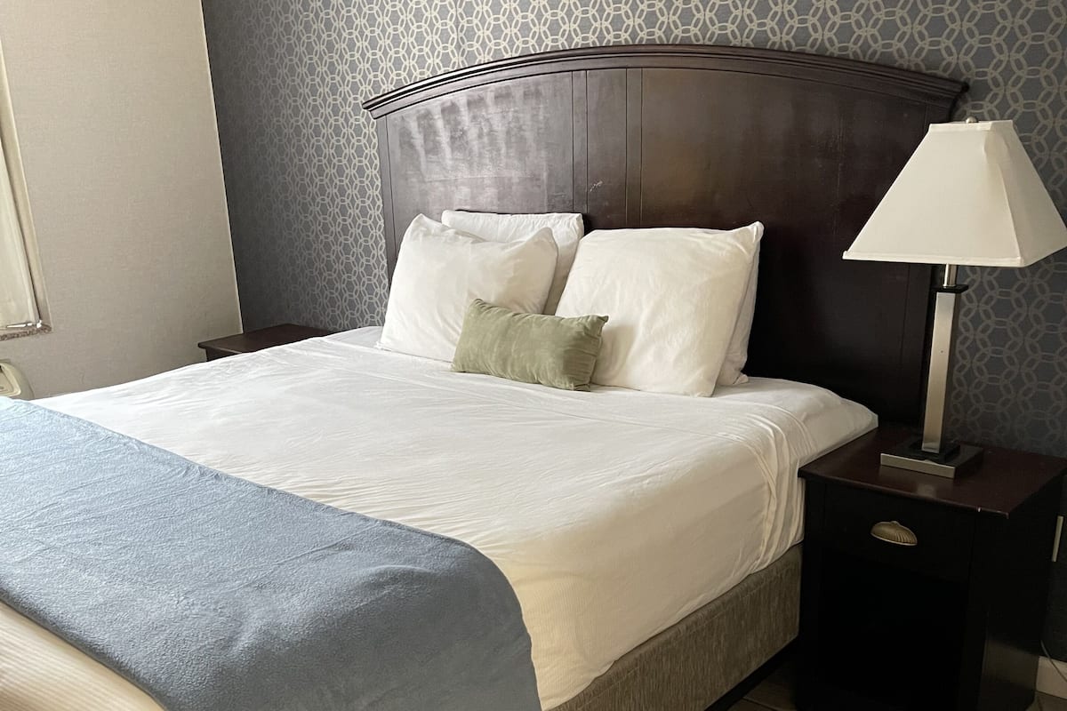 A neatly made bed with a grey blanket, a wooden headboard, and a bedside table with a lamp.