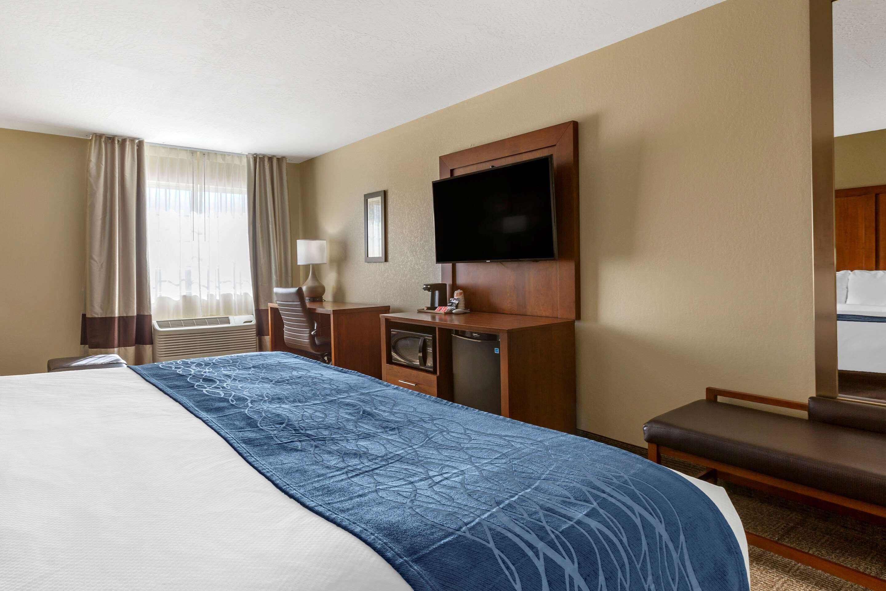 A hotel room with a large bed, a desk with a flat-screen TV, a microwave, and a refrigerator.